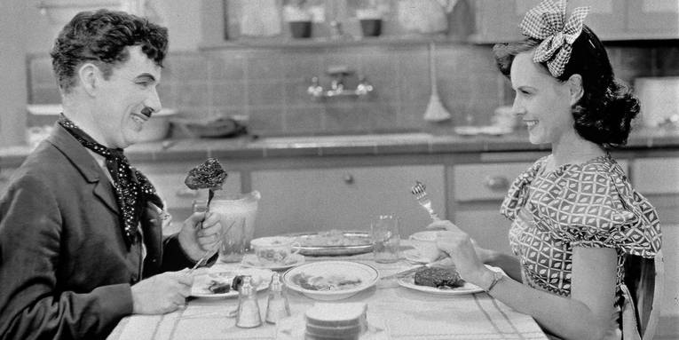 ein Mann und eine Frau sitzen am Tisch und essen. Sie schauen sich lächelnd an.